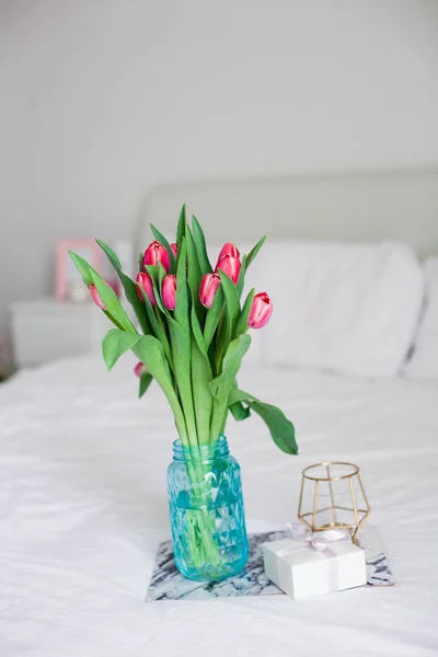 Intérieur. Chambre à coucher. Un bouquet de tulipes dans un vase en verre, une bougie, un plateau, une boîte avec un support cadeau sur le lit. Bonjour. Le printemps. L'été. Des vacances. Journée internationale de la femme. Fête des mères . — Photo