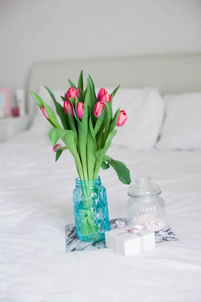 Home interior. Bedroom. A bouquet of tulips in a glass vase, a candle, a tray, a box with a gift stand on the bed. Morning. Spring. Summer. Holidays. International Womens Day. Mothers Day. — Stock Photo, Image