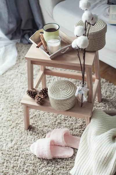 Decoração de casa. Uma mesa de cabeceira de madeira, um sofá, um algodão, uma caneca de café quente, uma xadrez de malha. Casa quente. Outono. Aconchegante. Casa. O livro e os óculos. Interior . — Fotografia de Stock