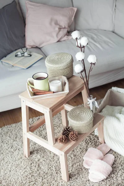 Decoración del hogar. Una mesita de noche de madera, un sofá, un algodón, una taza de café caliente, un tejido a cuadros. Casa cálida. Otoño. Acogedor. Casa. El libro y las gafas. Interior . —  Fotos de Stock