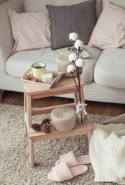 Decoración del hogar. Una mesita de noche de madera, un sofá, un algodón, una taza de café caliente, un tejido a cuadros. Casa cálida. Otoño. Acogedor. Casa. El libro y las gafas. Interior . — Foto de Stock