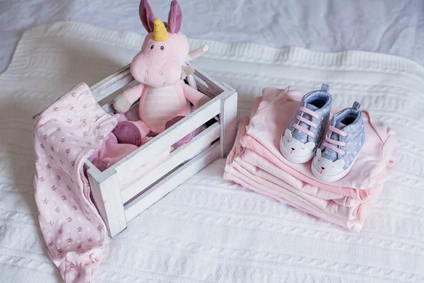 Children's shoes and clothes on the bed. Beautiful pink baby clothes. Newborn. Home cosiness. Baby.