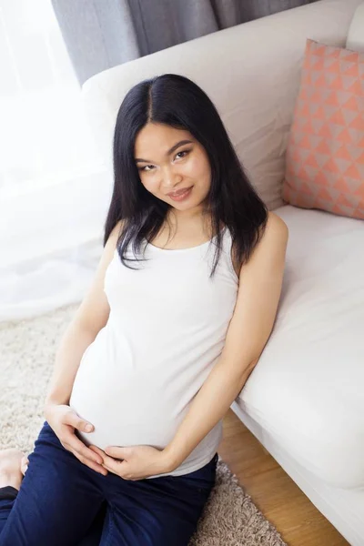 Güzel genç Asyalı hamile kadın pencerenin kenarında oturur ve karnı dokunur. Gebelik. Sağlık. Annelik. Hamile bir kadın rahat bir portresi. Rahat. — Stok fotoğraf