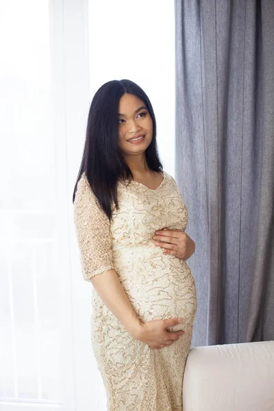 Pencerenin kenarında duran ve karnı dokunmadan güzel genç Asyalı hamile kadın. Gebelik. Sağlık. Annelik. Hamile bir kadın rahat bir portresi. Rahat. — Stok fotoğraf