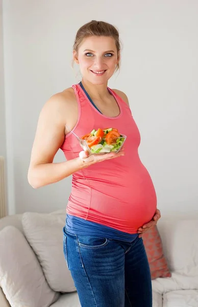 Młoda piękna kobieta w ciąży jest jedzenie Sałatka jarzynowa. Dziewczyna trzyma talerz sałatkowy. Zdrowe odżywianie. Ciąży. Macierzyństwo. Zdrowie. — Zdjęcie stockowe