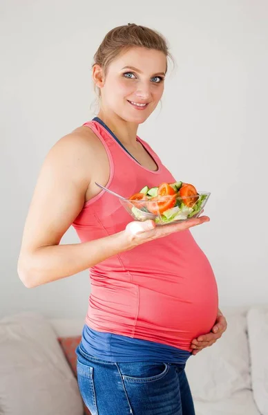 Genç güzel hamile kadın sebze salatası yiyor. Kız bir tabak salata tutuyor. Sağlıklı beslenme. Gebelik. Annelik. Sağlık. — Stok fotoğraf