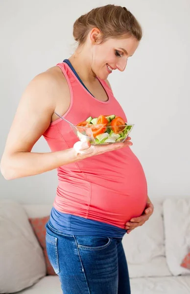 Jovem bela mulher grávida está comendo salada de legumes. A rapariga está a segurar um prato de salada. Alimentação saudável. Gravidez. Maternidade. Saúde . — Fotografia de Stock