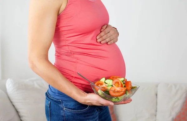 若い美しい妊娠中の女性は、野菜サラダを食べています。女の子はサラダのプレートを保持しています。健康的な食事。妊娠。母性。健康. — ストック写真