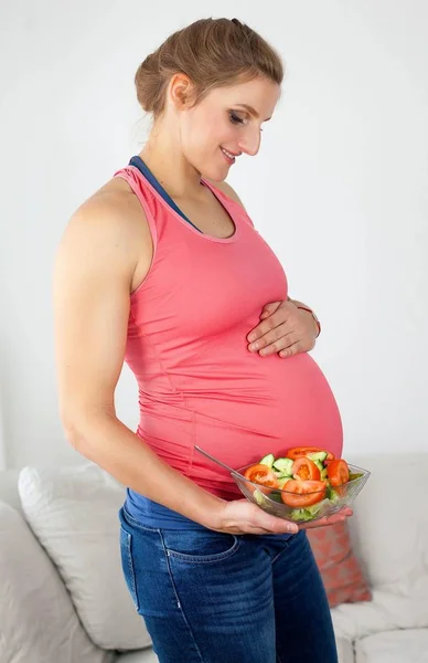 Junge schöne schwangere Frau isst Gemüsesalat. Das Mädchen hält einen Teller Salat in der Hand. Gesunde Ernährung. Schwangerschaft. Mutterschaft. Gesundheit. — Stockfoto