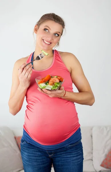 Junge schöne schwangere Frau isst Gemüsesalat. Das Mädchen hält einen Teller Salat in der Hand. Gesunde Ernährung. Schwangerschaft. Mutterschaft. Gesundheit. — Stockfoto