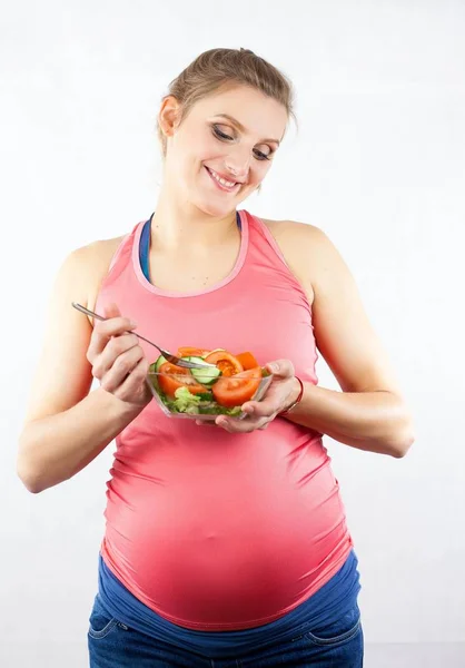 Young beautiful pregnant woman is eating vegetable salad. The girl is holding a plate of salad. Healthy eating. Pregnancy. Motherhood. Health. — Stock Photo, Image