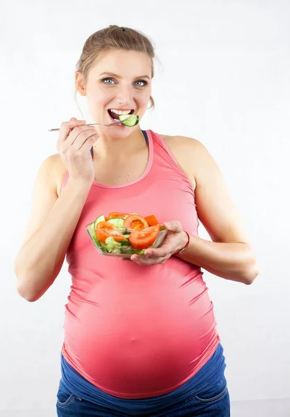 Young beautiful pregnant woman is eating vegetable salad. The girl is holding a plate of salad. Healthy eating. Pregnancy. Motherhood. Health. — Stock Photo, Image