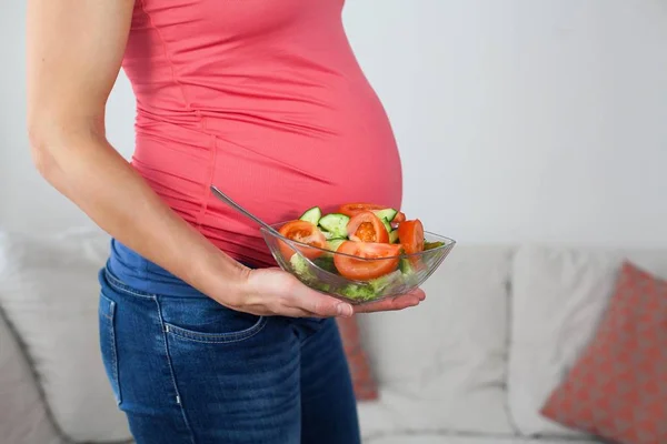 Young beautiful pregnant woman is eating vegetable salad. The girl is holding a plate of salad. Healthy eating. Pregnancy. Motherhood. Health. Stock Picture