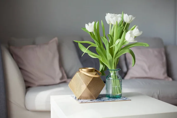 Interior. Room. A bouquet of tulips in a glass vase, a gold candlestick on a white wooden table. Sofa, pillows. Spring. It's cozy. Living room. — Stock Photo, Image