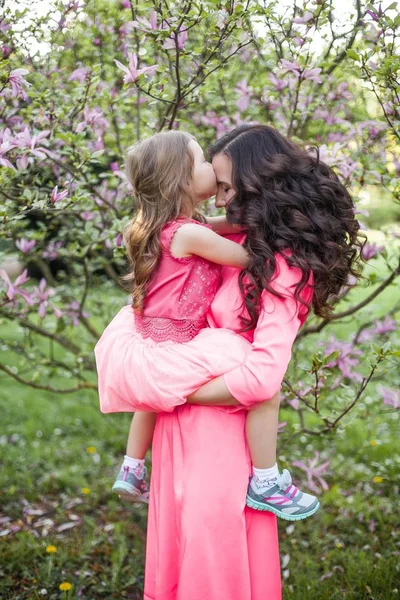 Молода красива мати з маленькою донькою йде вздовж весняного парку. Портрет матері і маленької дочки біля квітучої магнолії. Весна. Щаслива сім'я. Теплові . — стокове фото