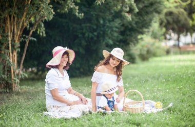 Genç bir anne, büyükanne ve küçük oğlu bir takas oynuyorlar. Piknik. Bahar. Yaz. Isı. Aile çimlerde oturuyor.