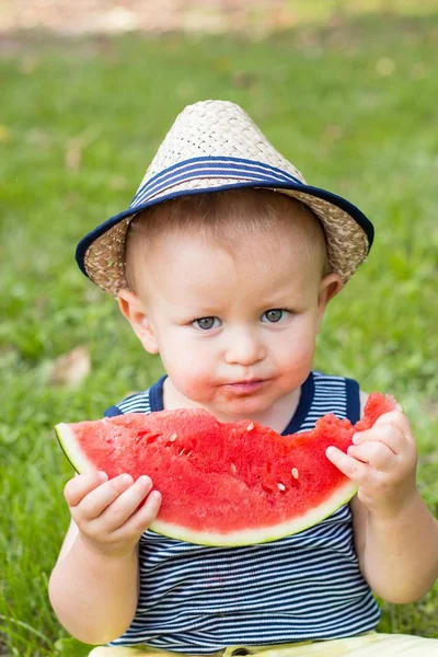 Un niño lindo está sentado en la hierba y comiendo una sandía. Picnic. El chico está descansando en el parque. Retrato de un niño pequeño. Una familia. Felicidad. Amor. . —  Fotos de Stock