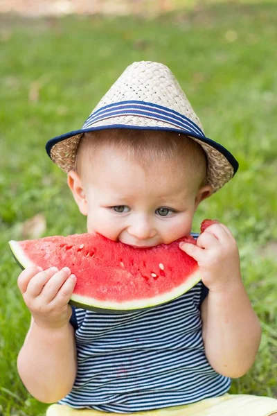 Un niño lindo está sentado en la hierba y comiendo una sandía. Picnic. El chico está descansando en el parque. Retrato de un niño pequeño. Una familia. Felicidad. Amor. . —  Fotos de Stock