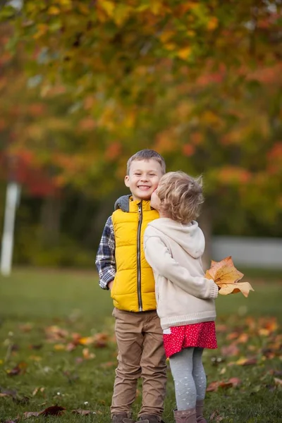 En liten pojke kramar en flicka. Porträtt av glada barn i ljusa höstkläder. Varm och ljus höst. — Stockfoto