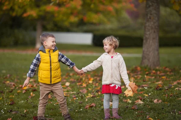 小男孩抱着一个女孩。 穿着鲜艳的秋天衣服的快乐孩子的画像。 温暖明亮的秋天. — 图库照片