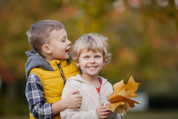 En liten pojke kramar en flicka. Porträtt av glada barn i ljusa höstkläder. Varm och ljus höst. — Stockfoto