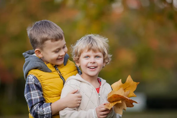小男孩抱着一个女孩。 穿着鲜艳的秋天衣服的快乐孩子的画像。 温暖明亮的秋天. — 图库照片