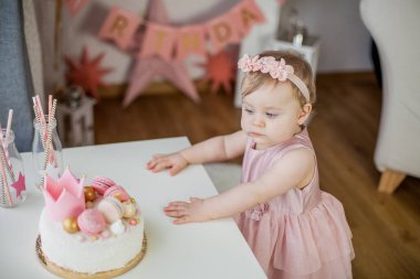 İlk doğum günüm. Pembe elbiseli küçük güzel kız doğum günü pastasını deniyor. Doğum günü partisi.