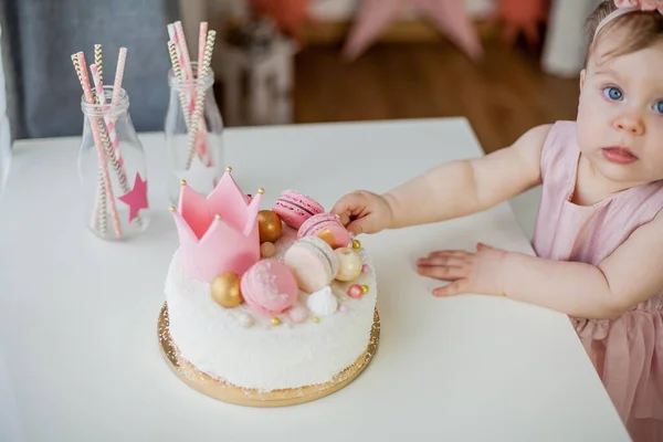 First birthday. Little beautiful girl in a pink dress tries her birthday cake. Birthday party.