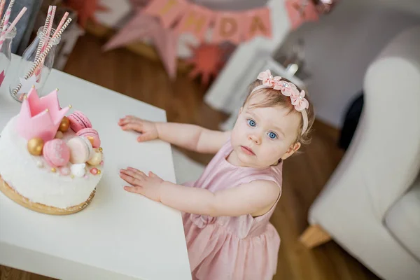 First birthday. Little beautiful girl in a pink dress tries her birthday cake. Birthday party.