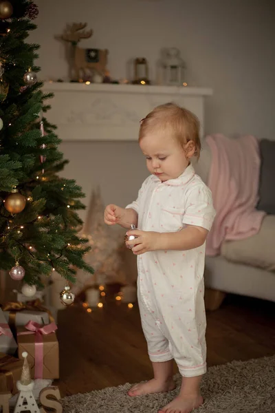 Little cute girl of 2 years in pajamas decorates a Christmas tree. Christmas. New Year. Holidays. Cozy. — Stock Photo, Image