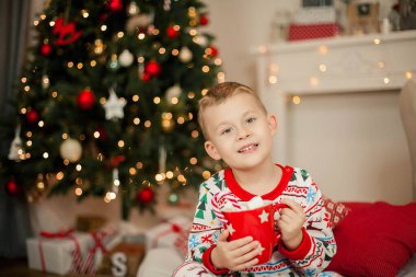Noel pijamalı küçük bir çocuk Noel ağacının yanında oturuyor ve elinde bir kupa marşmelovlu kakao tutuyor. Noel zamanı. Yeni Yıl.