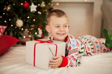 Noel pijamalı küçük bir çocuk Noel ağacının yanında oturur ve hediyeleri açar. Noel zamanı. Yeni Yıl.