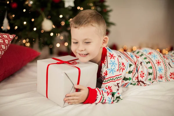 Маленький хлопчик у різдвяній піжамі сидить біля ялинки і відкриває подарунки. Різдво. Новий рік . — стокове фото