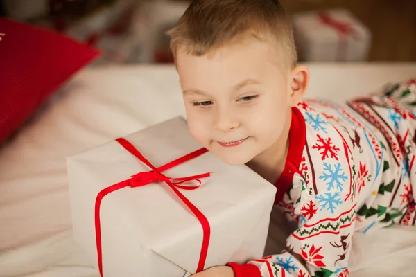 Um garotinho de pijama de Natal se senta perto de uma árvore de Natal e abre presentes. No Natal. Ano Novo . — Fotografia de Stock