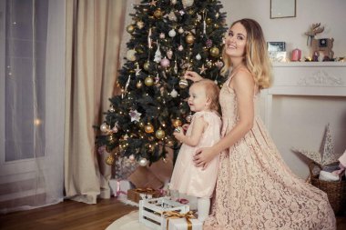 Güzel ve mutlu bir anne Noel ağacının yanında küçük bir kız çocuğunu tutuyor. Noel zamanı. Yeni Yıl.