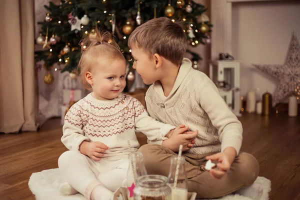 크리스마스 트리 근처에 앉아 크리스마스 쿠키와 우유를 마시는 귀여운 소년 과 소녀. 크리스마스. 새해. — 스톡 사진