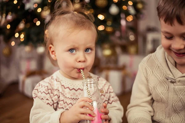 Piccolo ragazzo carino felice e ragazza sedersi vicino all'albero di Natale e bere latte con biscotti di Natale. Natale. Anno nuovo . — Foto Stock