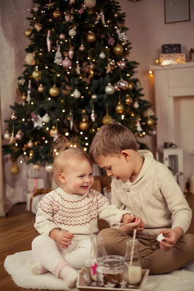 크리스마스 트리 근처에 앉아 크리스마스 쿠키와 우유를 마시는 귀여운 소년 과 소녀. 크리스마스. 새해. — 스톡 사진