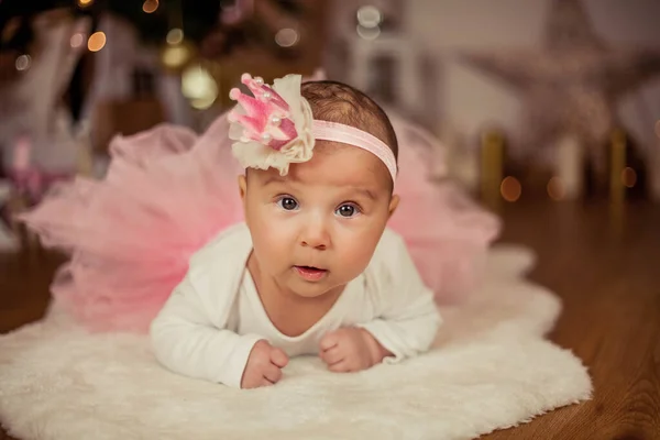 En tre månader gammal bebis i prinsessdräkt ligger på magen nära julgranen. Julen. Nytt år. — Stockfoto