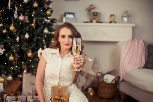 Uma bela jovem senta-se junto a uma árvore de Natal e abre presentes. No Natal. Ano Novo. Aconchegante . — Fotografia de Stock