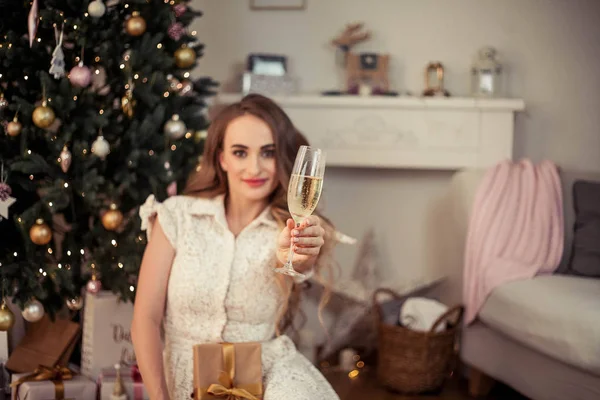Uma bela jovem senta-se junto a uma árvore de Natal e abre presentes. No Natal. Ano Novo. Aconchegante . — Fotografia de Stock