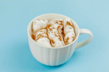 Kakaolu ve şekerli büyük beyaz bir kupa, mavi arka planda tarçın. Noel nedenleri. Geleneksel kış içeceği.