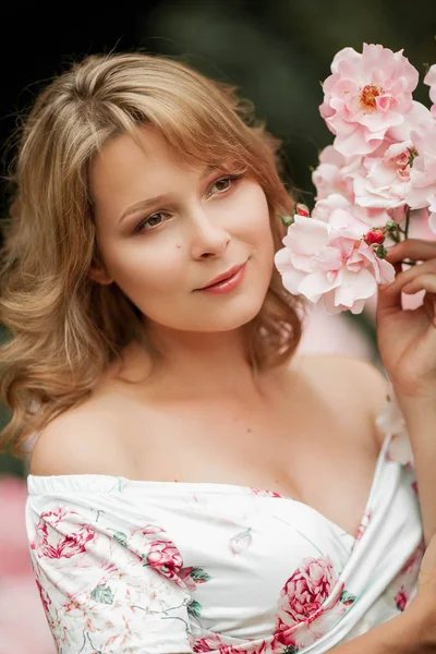 Uma bela jovem grávida está andando em um jardim de rosas. Retrato de uma mulher grávida em um vestido. Verão . — Fotografia de Stock