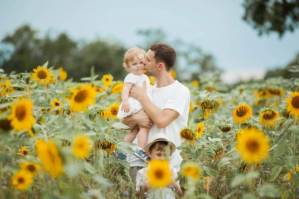 幸せな家族がひまわり畑を歩いています。ひまわり畑に2人の子供を持つ若いハンサムなお父さん. — ストック写真