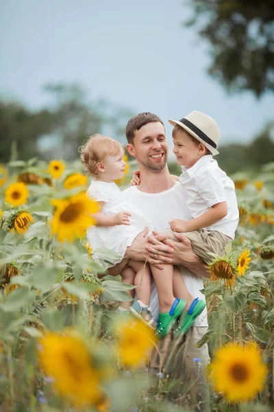 Szczęśliwa rodzina spaceruje po polu słoneczników. Młody przystojny tata z dwójką dzieci na polu słonecznika. — Zdjęcie stockowe