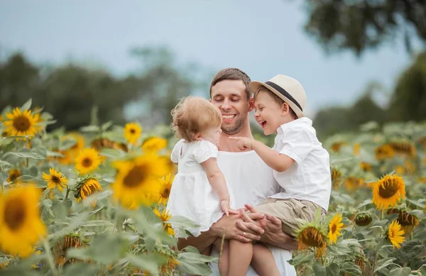 Szczęśliwa rodzina spaceruje po polu słoneczników. Młody przystojny tata z dwójką dzieci na polu słonecznika. — Zdjęcie stockowe