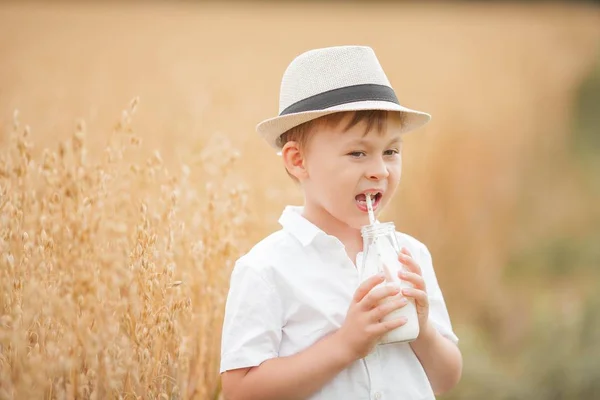 Portrét chlapce na pšeničném poli. Chlapec pije mléko ze skleněné láhve. — Stock fotografie