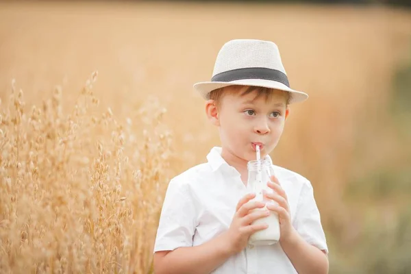 Portrét chlapce na pšeničném poli. Chlapec pije mléko ze skleněné láhve. — Stock fotografie