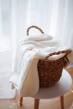 Çarşaflı hasır sepet pencerede duruyor. Örgü süveter, yılbaşı ışıkları. Samimi.