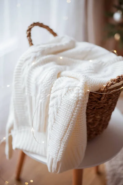 Un cestino di vimini con supporti di lino alla finestra. Maglione lavorato a maglia, luci di Natale. Accogliente . — Foto Stock